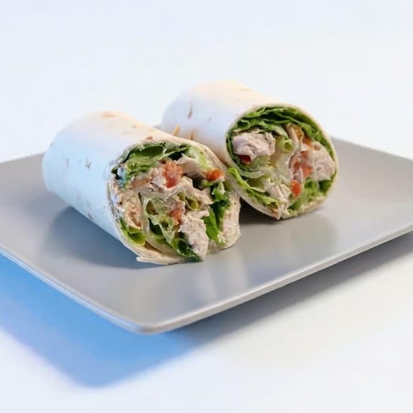 Two chicken wraps, filled with lettuce and tomatoes, on a gray rectangular plate.