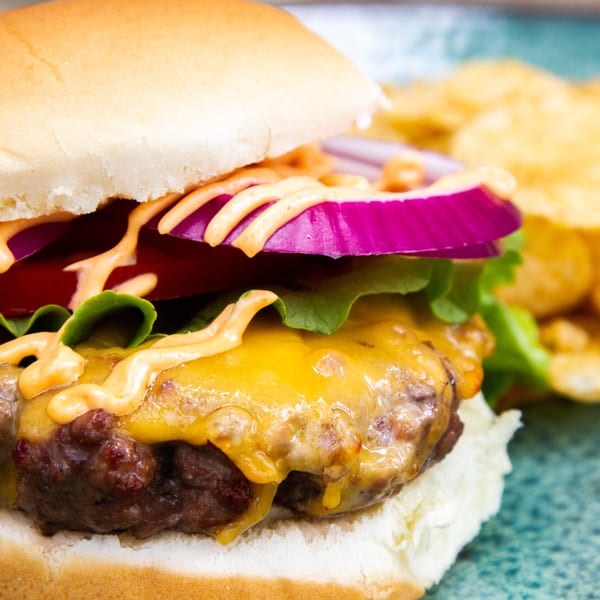 Close-up of a cheeseburger with red onion, lettuce, and special sauce, served with chips.