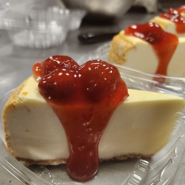 Two slices of cheesecake with strawberry topping in clear plastic containers.