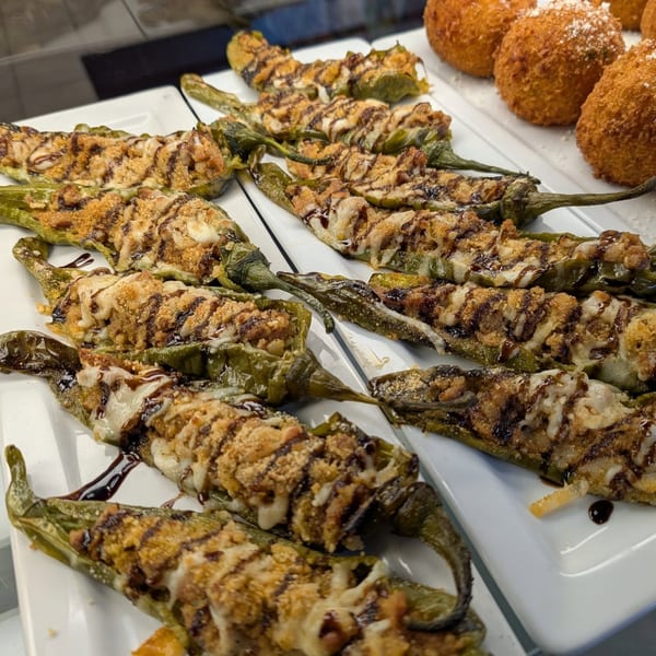 Plates of stuffed green peppers with melted cheese and balsamic glaze, alongside arancini balls.