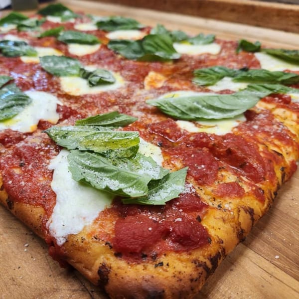 Tony's Pizzeria's rectangular pizza with fresh basil, mozzarella, and tomato sauce on a wooden board.